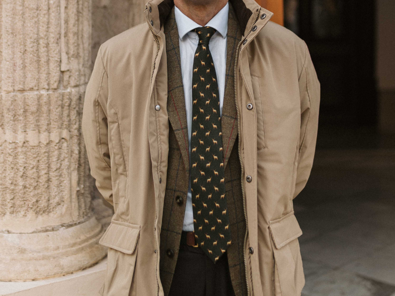 Hombre luciendo una corbata de lana verde con estampado de ciervos, combinada con una americana de tweed y chaqueta beige.